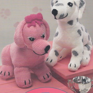 May include: Two knitted stuffed animals, a pink poodle with a pink bow and a white dalmatian with black spots. The animals are sitting on a pink surface with a silver trophy in the foreground. The text "Puppy in my pocket" is printed below the animals.