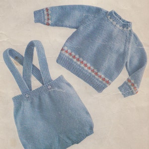 Könnte beinhalten: Ein gestricktes Baby-Outfit in Blau, bestehend aus einem Pullover und einer Latzhose. Der Pullover hat einen weißen und roten Besatz am Hals und an den Ärmeln. Die Latzhose hat Träger, die an den Schultern geknöpft werden.