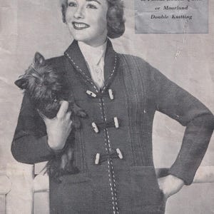 May include: A dark gray knitted cardigan with white stitching and toggle closures. The cardigan has a shawl collar and a pocket. The image also includes a small dog and text that reads "in Patons Double Quick or Moorland Double Knitting."