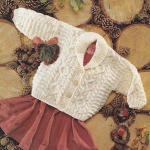 Puede incluir: Rebeca de punto color crema con cuello y cierre de botones. El suéter presenta una aplicación decorativa y se combina con una falda roja. El fondo incluye piñas y rodajas de madera, lo que sugiere un tema rústico y acogedor.