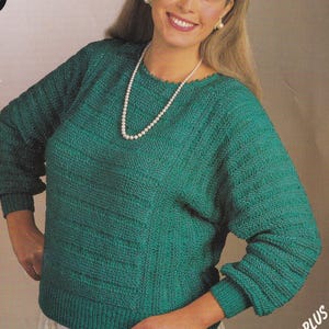 May include: A green knitted jumper with long sleeves, a ribbed hem, and a textured pattern. The pattern packaging displays the text JX122 DK, 38-56in, 97-143cm, and SIZED FOR 38" PLUS. The jumper features a round neckline and a consistent knit stitch.