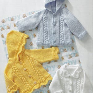 May include: Three knitted baby cardigans in blue, yellow and white with button fastenings and hoods. The cardigans feature a cable knit design.