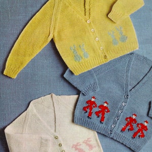 Puede incluir: Tres cárdigans de punto en amarillo, azul y blanco roto. Cada cárdigan presenta un cuello en V, cierre de botones y un patrón decorativo de conejos o figuras. El cárdigan amarillo tiene conejos verdes, el azul tiene figuras rojas y el blanco roto tiene conejos rosas.