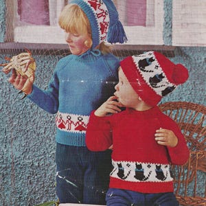 Könnte beinhalten: Zwei Kinder tragen gestrickte Pullover und Mützen mit einem Winterfest-Motiv. Das Mädchen trägt einen blauen Pullover mit rotem und weißem Besatz und eine rote und weiße Mütze mit einem blauen Bommel. Der Junge trägt einen roten Pullover mit weißem und schwarzem Besatz und eine rote und weiße Mütze mit einem weißen Bommel.