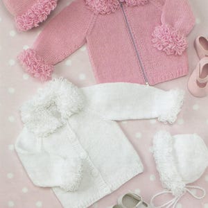 May include: Two knitted baby jackets with matching hats. One jacket is pink with a zipper closure and the other is white with button closures. Both jackets have fluffy collars and cuffs.