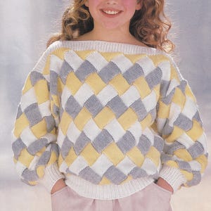 May include: A knitted sweater with a geometric pattern in white, yellow, and gray. The sweater has a boat neck and long sleeves.