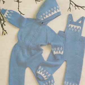 May include: A blue knitted baby jumpsuit with a white snowflake pattern on the sleeves and legs. The jumpsuit has a hood and a zipper closure. There is also a matching pair of blue knitted overalls with a white snowflake pattern on the chest.