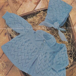 May include: A light blue knitted baby cardigan with a matching bonnet. The cardigan has a button closure and a collar. The bonnet has a bow.
