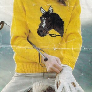 Peut inclure: Une jeune personne portant un pull jaune avec un motif de cheval brun, chevauchant un cheval blanc. La personne tient une cravache dans sa main et porte des gants blancs.