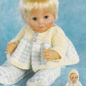 Puede incluir: Muñeca vestida con un conjunto tejido a mano en crema y azul claro. El conjunto incluye un suéter con dos botones decorativos, pantalones y un gorro a juego. La muñeca mide aproximadamente 25-30 cm de alto.