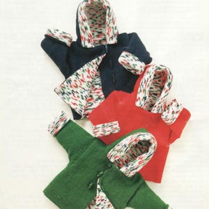 May include: Three miniature hooded jackets in navy blue, red, and green. Each jacket features a contrasting patterned lining and cuffs with red, green, and white accents. The jackets are arranged in a layered composition.