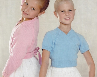 May include: Two young girls wearing ballet attire. One girl is wearing a light pink wrap sweater and a white skirt. The other girl is wearing a light blue wrap sweater and a white skirt. Both girls are smiling.