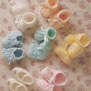 May include: A collection of knitted baby booties in pastel shades: white, pale blue, pink, peach, and yellow. Some have ribbon fastenings, others floral embroidery. The booties are displayed on a floral patterned fabric background.