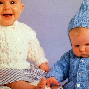 Op de afbeelding: Twee baby's dragen gebreide vesten. De baby aan de linkerkant draagt een wit vest met knopen en een gestreepte rok. De baby aan de rechterkant draagt een blauw vest met een puntige capuchon.