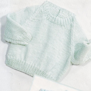 May include: A light blue knitted sweater with short sleeves. The sweater has a ribbed hem and cuffs, and a crew neck. The knitwear is a soft, pastel color, and the texture of the yarn is visible.