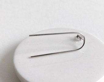May include: A silver earring with a small, clear stone at the end of a curved wire.