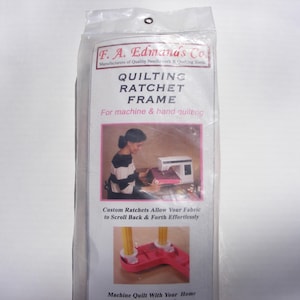 May include: A white and pink quilting frame with a ratchet system. The frame is designed for both machine and hand quilting. The packaging includes a photo of a person using the frame with a sewing machine.