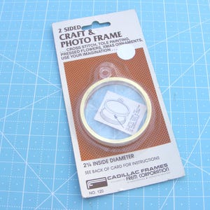 May include: A packaged craft and photo frame with a gold-colored circular frame. The package reads "2 SIDED CRAFT & PHOTO FRAME" and lists craft applications. The frame has a 2.25-inch inside diameter.