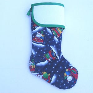 May include: A Christmas stocking with a navy blue background featuring a pattern of Santa Claus in a car, snow, and stars. The top is white with a green trim and a green loop for hanging.