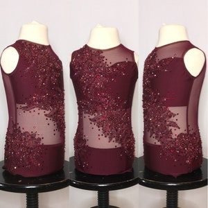 Könnte beinhalten: Burgunderfarbener Tanz-Leotard mit einem durchsichtigen Mesh-Überzug und aufwendigen roten Strass-Verzierungen.