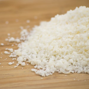 May include: A close-up of a pile of white coconut flakes on a wooden surface.
