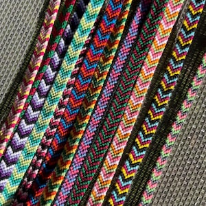 May include: A collection of colorful friendship bracelets. Each bracelet features a chevron pattern in various colors, including pink, green, yellow, blue, and purple. The bracelets are made of woven thread.