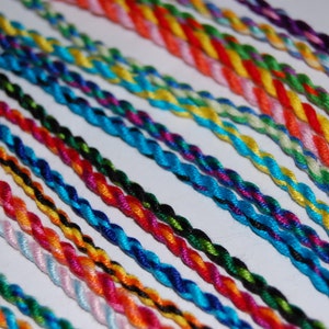 May include: A collection of colorful braided cords, each with a unique combination of colors. The cords are arranged in rows, with the ends of the cords extending to the right.