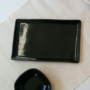 Puede incluir: Una bandeja rectangular negra para servir con un acabado brillante y un tazón negro más pequeño.