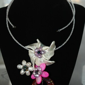 May include: A white and pink beaded necklace with a large white flower pendant and a smaller pink flower pendant. The pendant is made of shell and has a brown stone accent.