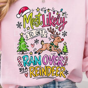 Peut inclure: Un sweat-shirt à manches longues rose clair avec une impression graphique colorée portant le texte Most Likely To Get Ran Over By A Reindeer. Le motif comprend un renne de dessin animé, un bonnet de Père Noël, des sapins et des sucres d'orge.