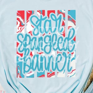 Könnte beinhalten: Hellblaues T-Shirt mit dem Text "Star Spangled Banner" in einem rot-weiß-blauen Design. Das Shirt wird mit Jeansshorts, einer weißen Baseballkappe und einer Tragetasche kombiniert.
