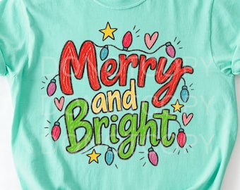 May include: A mint green short-sleeve t-shirt featuring the text Merry and Bright in red and green script. The design includes colorful hand-drawn style Christmas light bulbs, small yellow stars, and pink hearts surrounding the lettering.