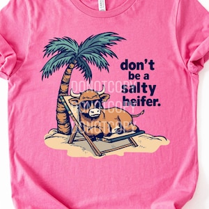 May include: Pink t-shirt featuring a cartoon cow wearing sunglasses, relaxing in a beach chair under a palm tree. The text "don't be a salty heifer" is printed on the shirt.