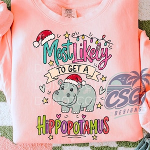 Peut inclure: Un sweat-shirt à col rond pêche clair avec un motif d'hippopotame gris portant un bonnet de Père Noël. Le texte indique Most Likely TO GET A HIPPOPOTAMUS, entouré de guirlandes lumineuses colorées, d'étoiles et de petits cœurs.