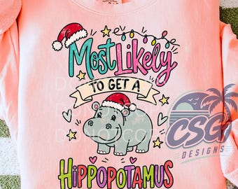 May include: A light peach-colored crewneck sweatshirt featuring a graphic of a gray hippopotamus wearing a Santa hat. The text reads Most Likely TO GET A HIPPOPOTAMUS, surrounded by colorful Christmas lights, stars, and small hearts.