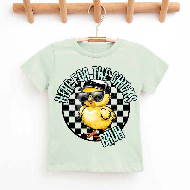 Puede incluir: Camiseta verde claro con un gr&aacute;fico de un pollito amarillo con gafas de sol y una gorra negra. El texto "HERE FOR THE CHICKS BRUH" est&aacute; impreso alrededor del pollito sobre un fondo a cuadros.