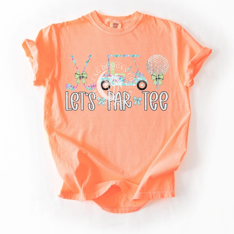 May include: Orange short-sleeved t-shirt with a golf cart, golf clubs, golf balls, and bows in a floral pattern. The text "Let's Par-Tee" is printed in white glitter on the shirt.