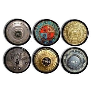 May include: A set of six circular metal objects featuring vintage safe dials and emblems. Two dials are marked Yale, one features a Phillips & Son Birmingham crest, one shows J. Cartwright & Sons, one is labelled Safe Six Levers, and one has an alphabet ring.