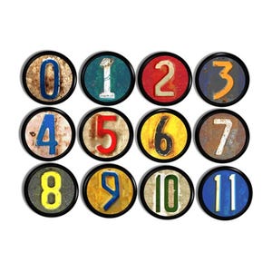 May include: A collection of twelve circular magnets, each displaying a number from 0 to 11. The numbers are in diverse colours and styles, set against a distressed, vintage backdrop. Each magnet has a black border.