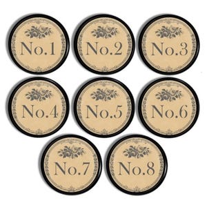 May include: Eight round, black-framed, cream-colored paper place cards with a floral design and the numbers 1 through 8 written in black.