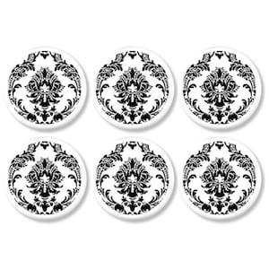 May include: Six white, circular coasters featuring a black damask design. Each coaster has a symmetrical floral pattern with swirling leaves and decorative elements. The coasters are arranged in a grid formation against a white backdrop.