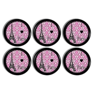 May include: Six round black coasters with a pink and white damask pattern. Each coaster features a black Eiffel Tower silhouette, a black heart, and the word "Paris" in white. The phrase "I ❤️ Paris" is also visible.
