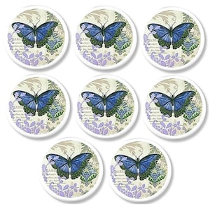 May include: Seven circular magnets with a blue butterfly design, green and purple details. The butterfly is set against a cream background with floral and text elements. The magnets are arranged in a grid pattern.