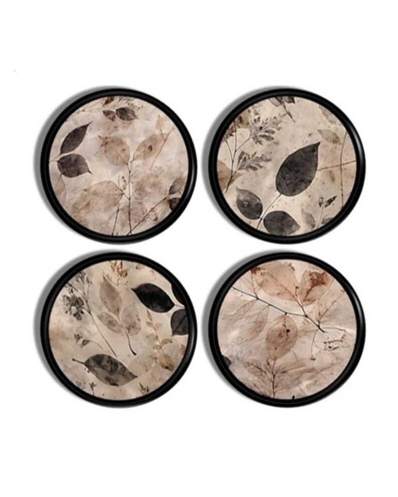 May include: A set of four circular coasters, each featuring a black frame and a beige background decorated with a botanical print of various dark brown and tan leaves and twigs. The designs on each coaster vary, showcasing different leaf arrangements.
