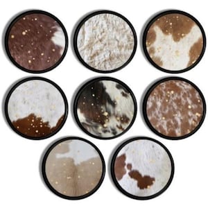 Könnte beinhalten: Acht runde Wanddekorationen mit schwarzen Rahmen und einem Muster aus weißem, braunem und goldenem Kuhfell.