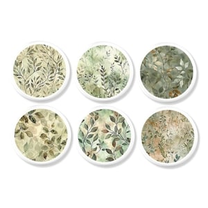 May include: Six round coasters with white borders, each featuring a different watercolor design of green and brown leaves. The coasters have a botanical theme and are arranged in two rows of three.