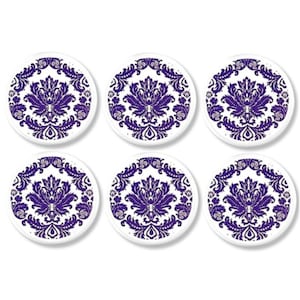 May include: Set of six white ceramic coasters with a purple damask pattern.