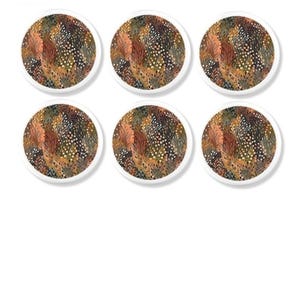 May include: A set of six circular coasters featuring a repeating pattern of stylised foliage in shades of burnt orange, deep brown, muted green, and cream. Each coaster has a clean white border and a flat, round shape for surface protection.