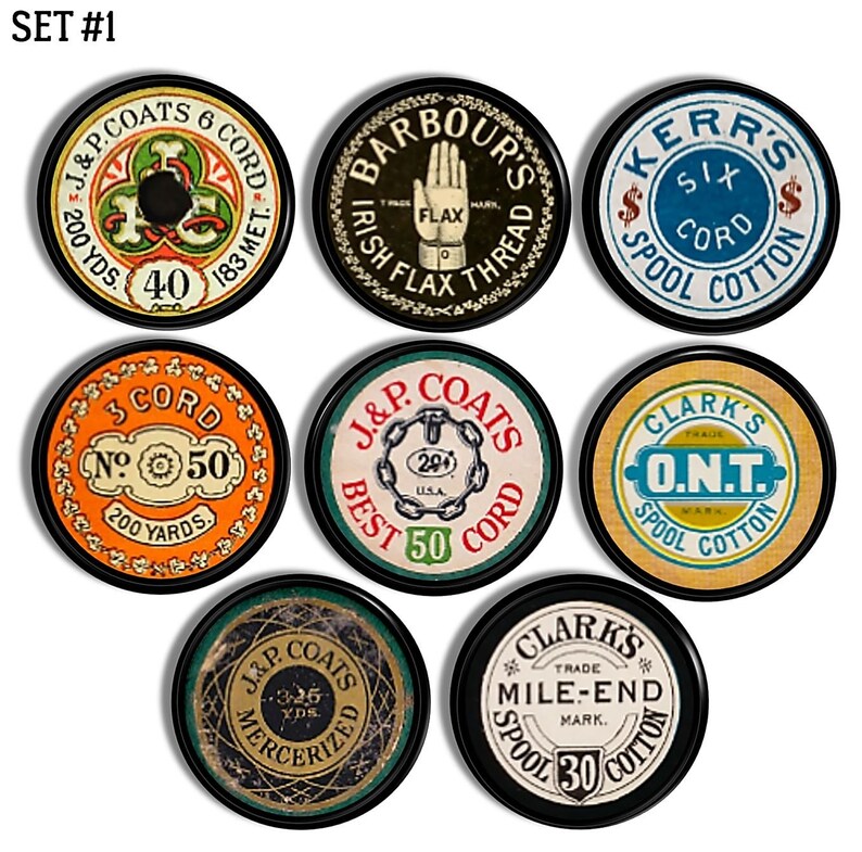 Op de afbeelding: Een set van negen vintage garenklossen met verschillende kleuren, ontwerpen en tekst. De klossen zijn rond en hebben een zwarte rand. De tekst op de klossen omvat "J&P Coats", "Barbour's Irish Flax Thread", "Kerr's Six Spool Cotton", "3 Cord No. 50 200 Yards", "Clark's O.N.T. Spool Cotton", "J&P Coats Best 50 Cord", "Clark's Trade Mile-End Mark. Spool 30 Cotton" en "J&P Coats 326 Yds. Mercerized".