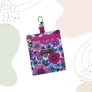 Pode incluir: Uma pequena bolsa com padrão floral, fecho de correr e fecho de metal dourado. A bolsa apresenta um design vibrante de flores rosa, roxas e azuis com folhas verdes. A marca "anjurisa" é exibida em uma pequena etiqueta dourada.